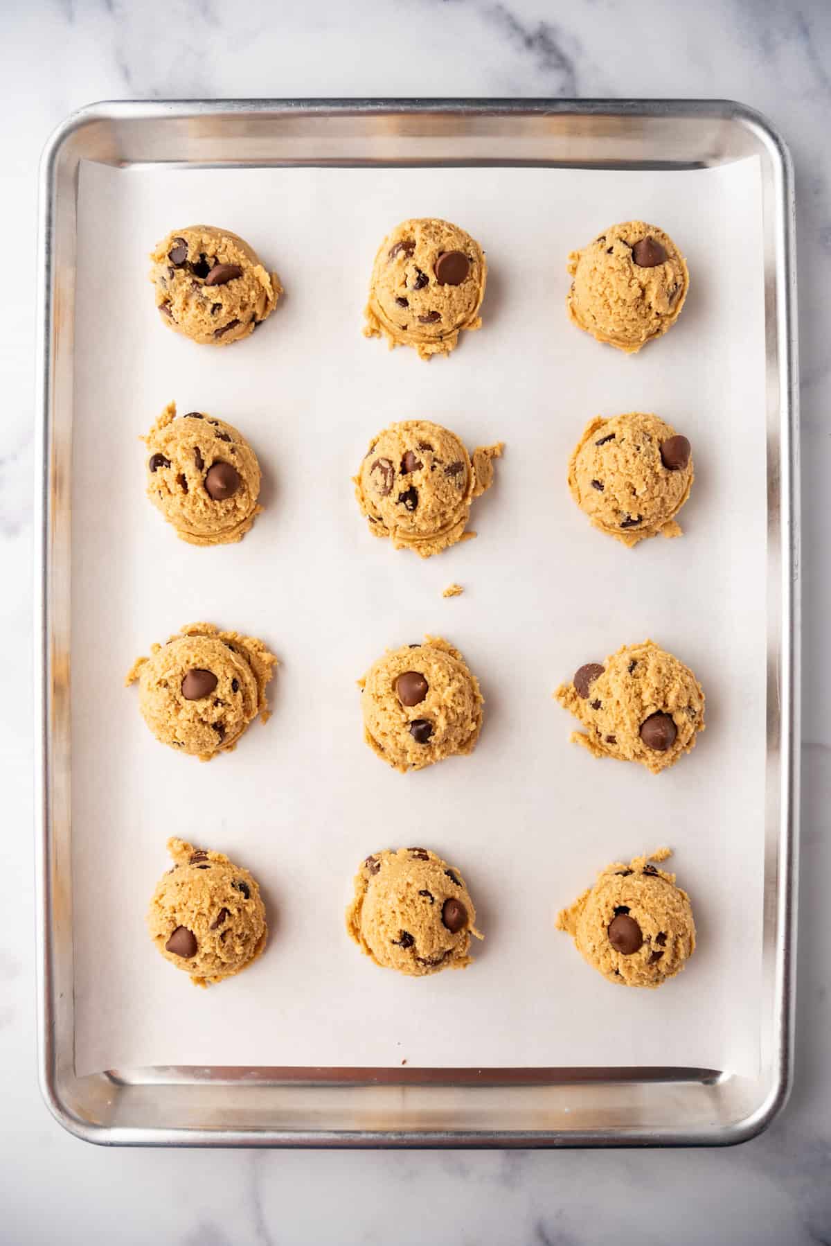 Unbaked balls of oatmeal peanut butter chocolate chip cookie dough on a baking sheet lined with parchment paper.