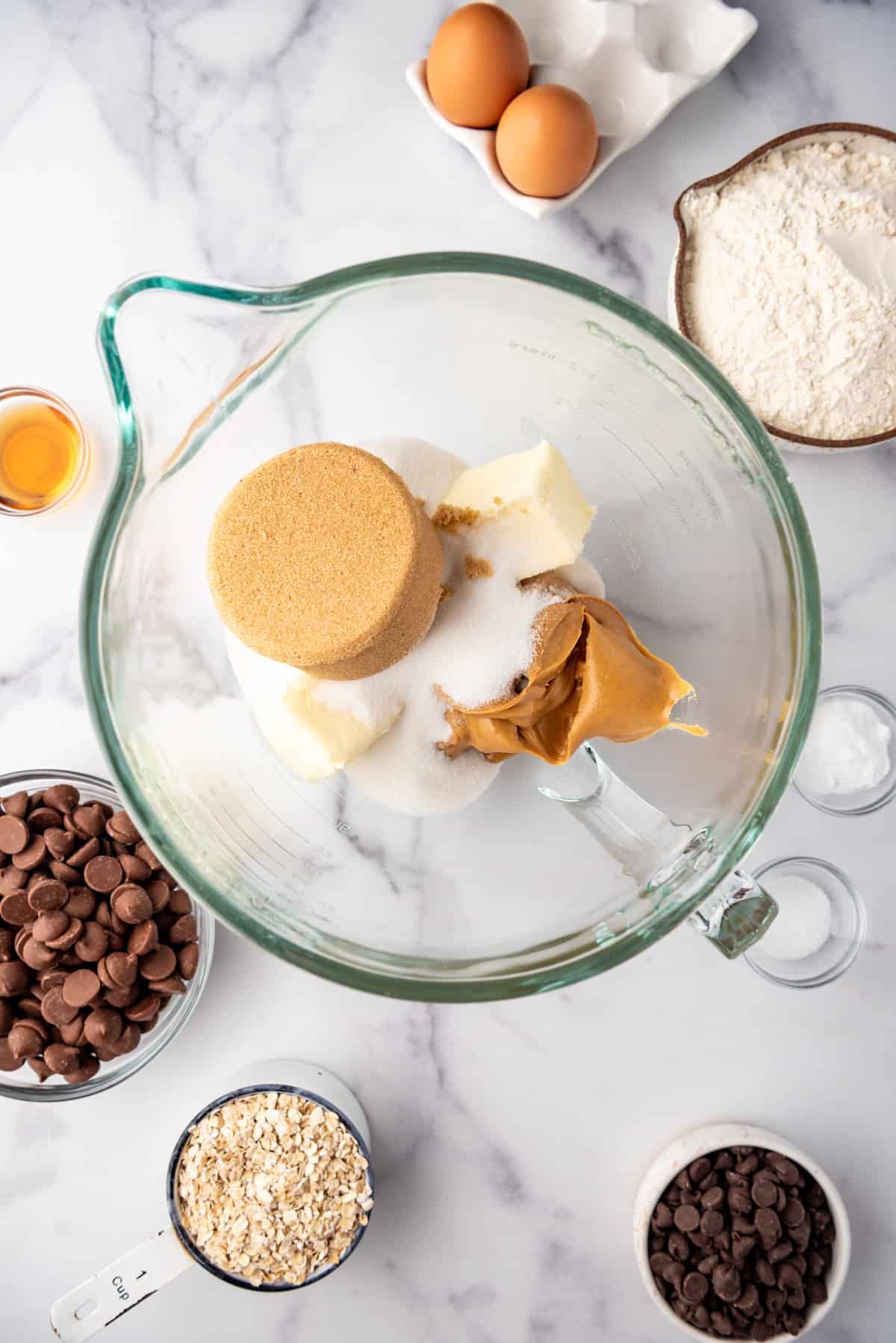 Combining softened butter, creamy peanut butter, and two types of sugar in a glass mixing bowl.