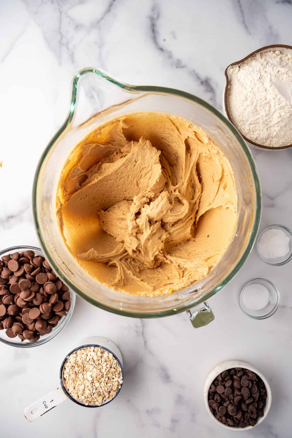 Creamy peanut butter cookie dough in a bowl surrounded by other ingredients.