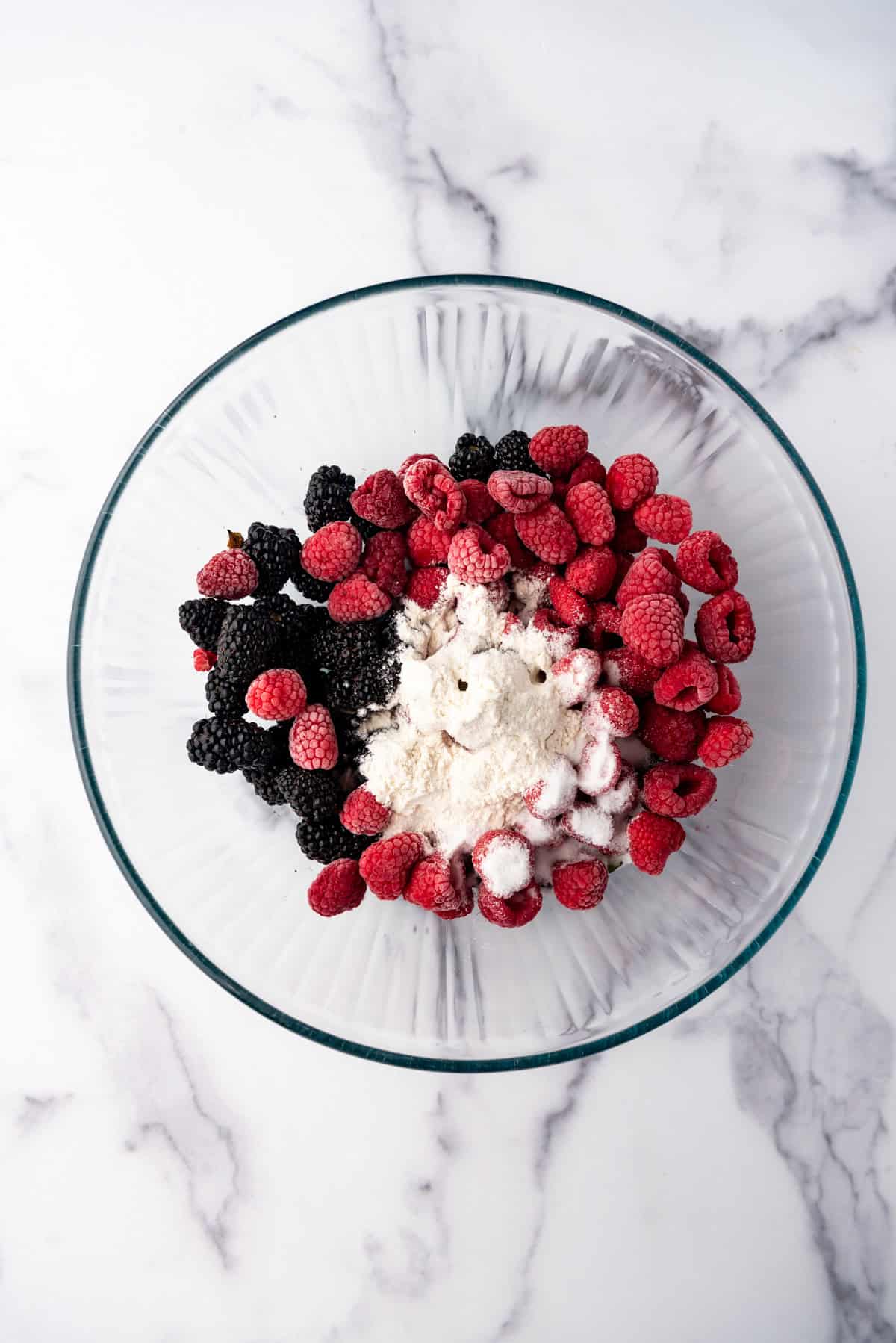 Combining blackberries and raspberries in a glass bowl with sugar and flour.