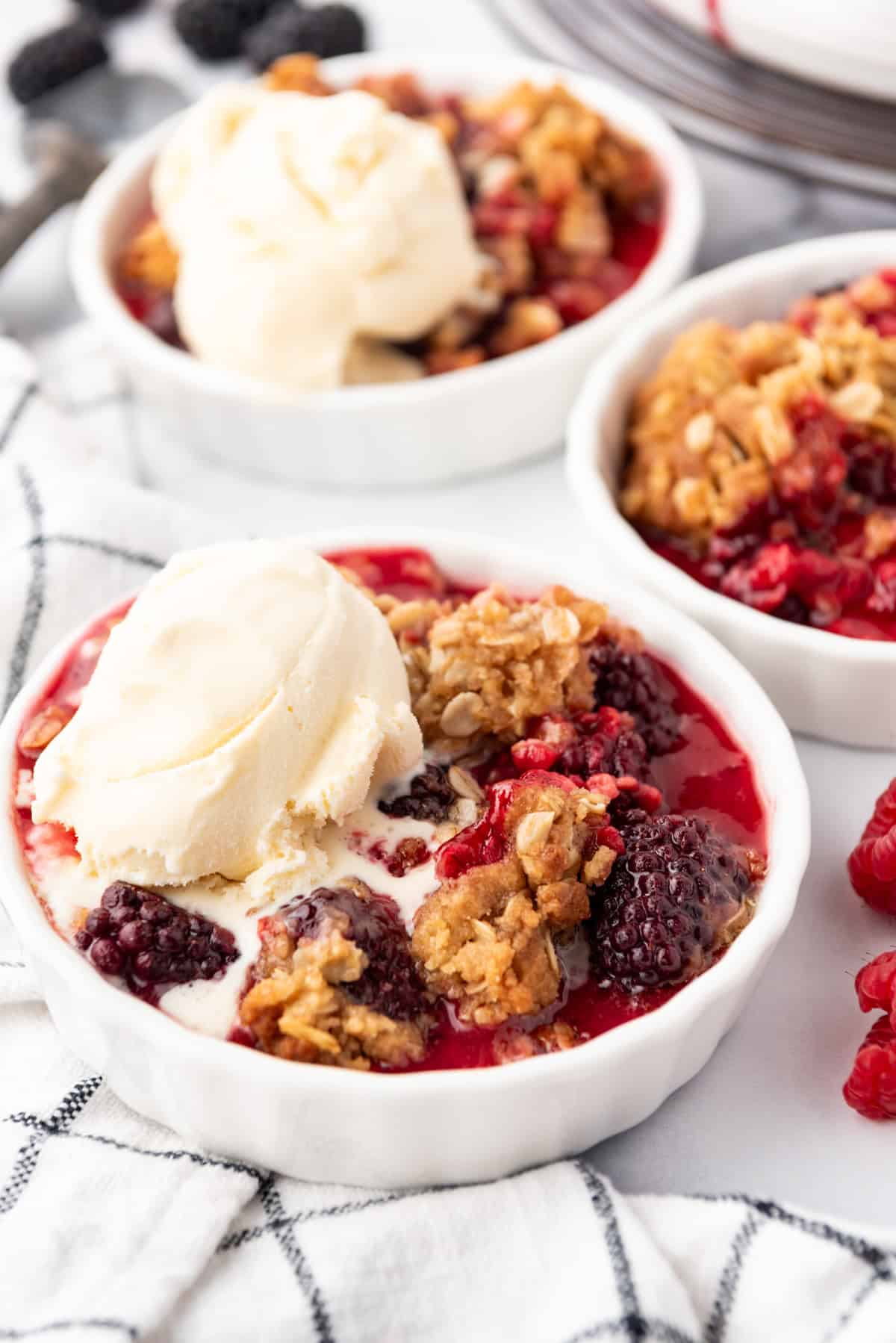 An image of individual berry crisp servings in white ramekins with vanilla ice cream on top.