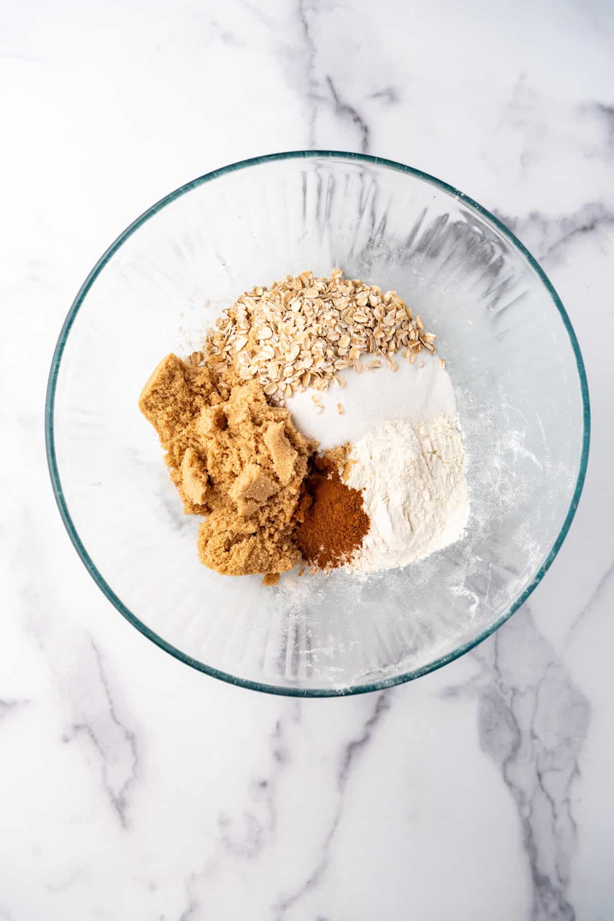 Combining flour, oats, sugar, and cinnamon in a mixing bowl.