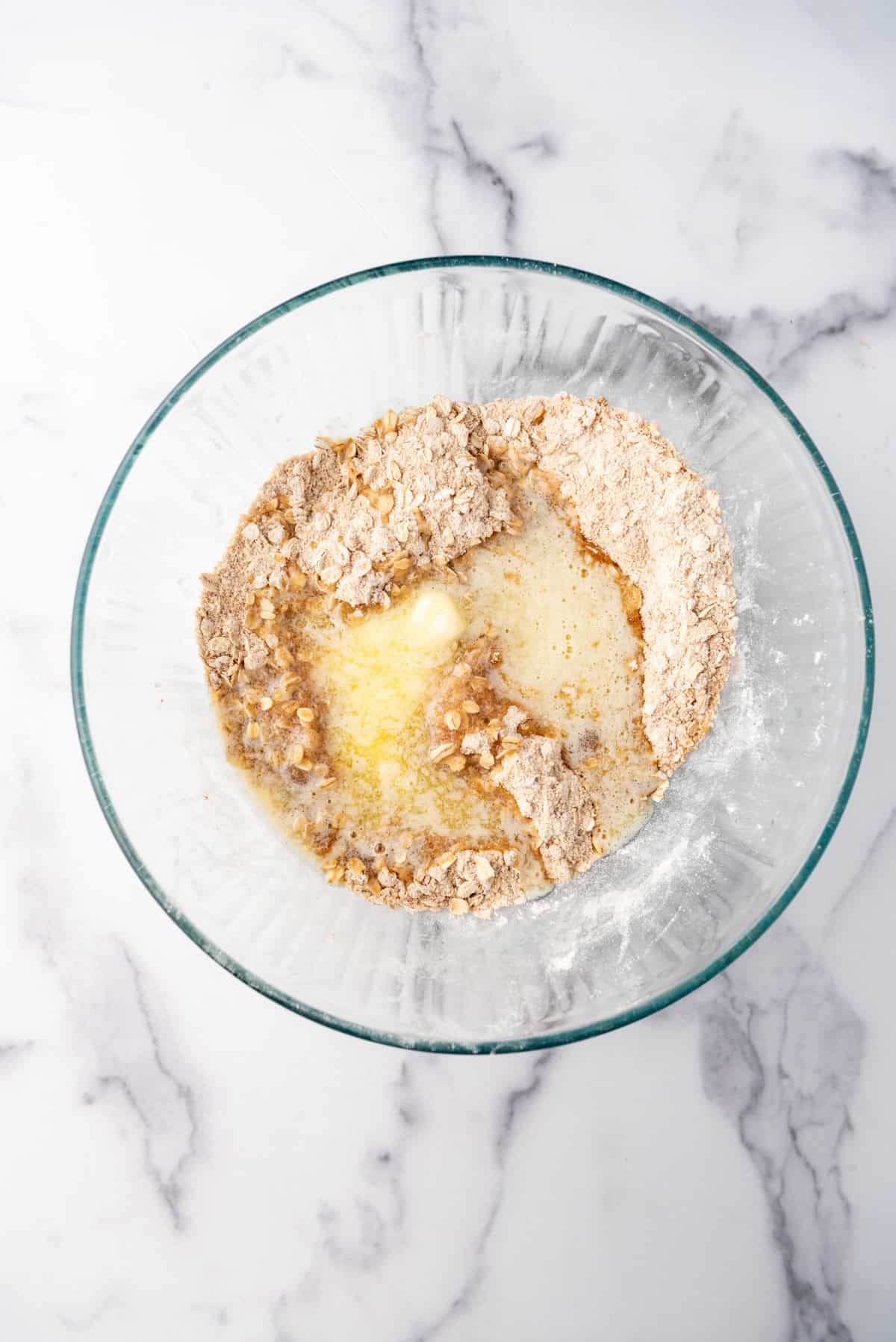 Adding melted butter to flour, oats, and sugar in a large mixing bowl.