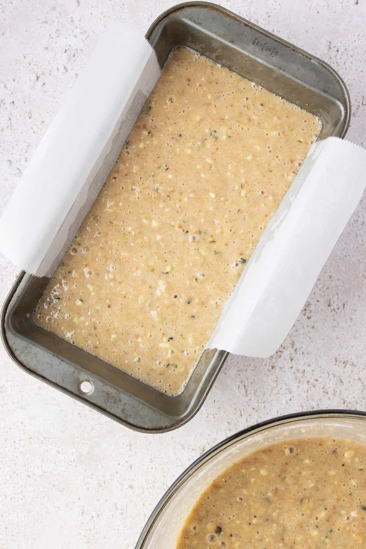 Pineapple zucchini bread batter in a loaf pan with a parchment paper sling.