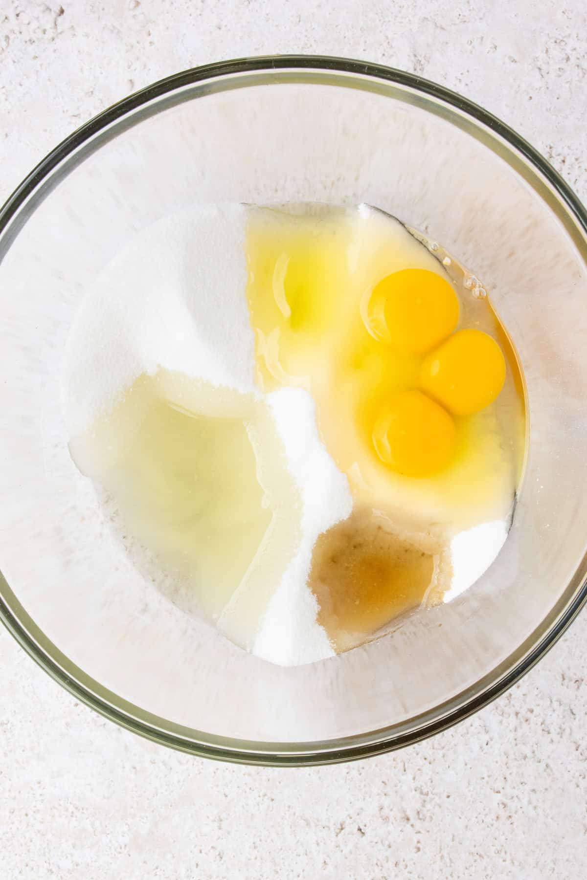 Combining sugar, oil, eggs, and vanilla in a large mixing bowl.