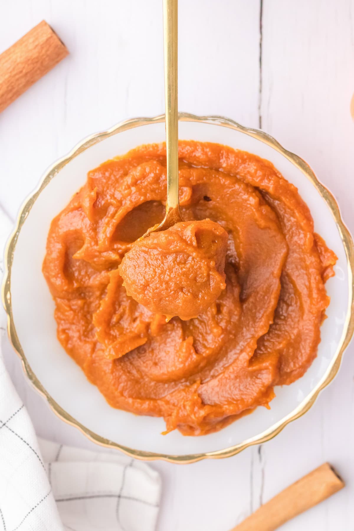 A brass spoon lifting pumpkin butter out of a bowl.