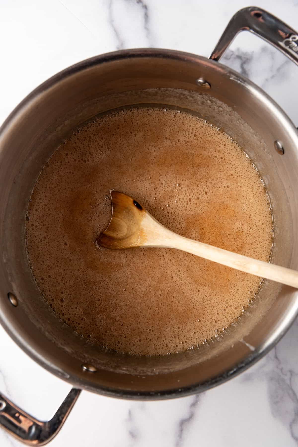 Finished creamy cinnamon syrup in a large pot with a wooden spoon.