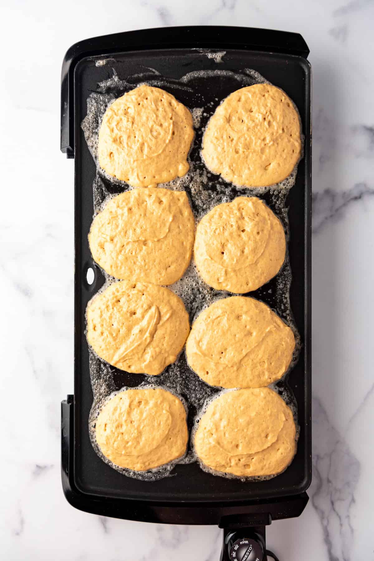 Pumpkin pancake batter cooking on a hot griddle.