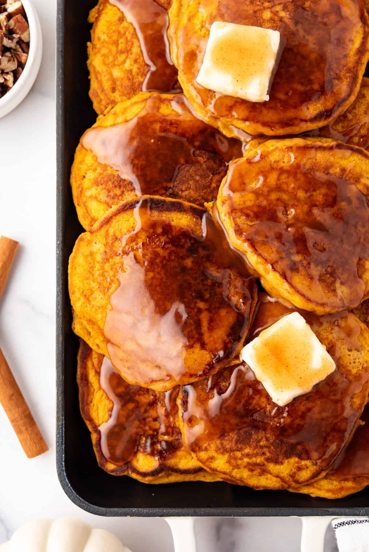 A close overhead image of pumpkin pancakes with syrup and butter.