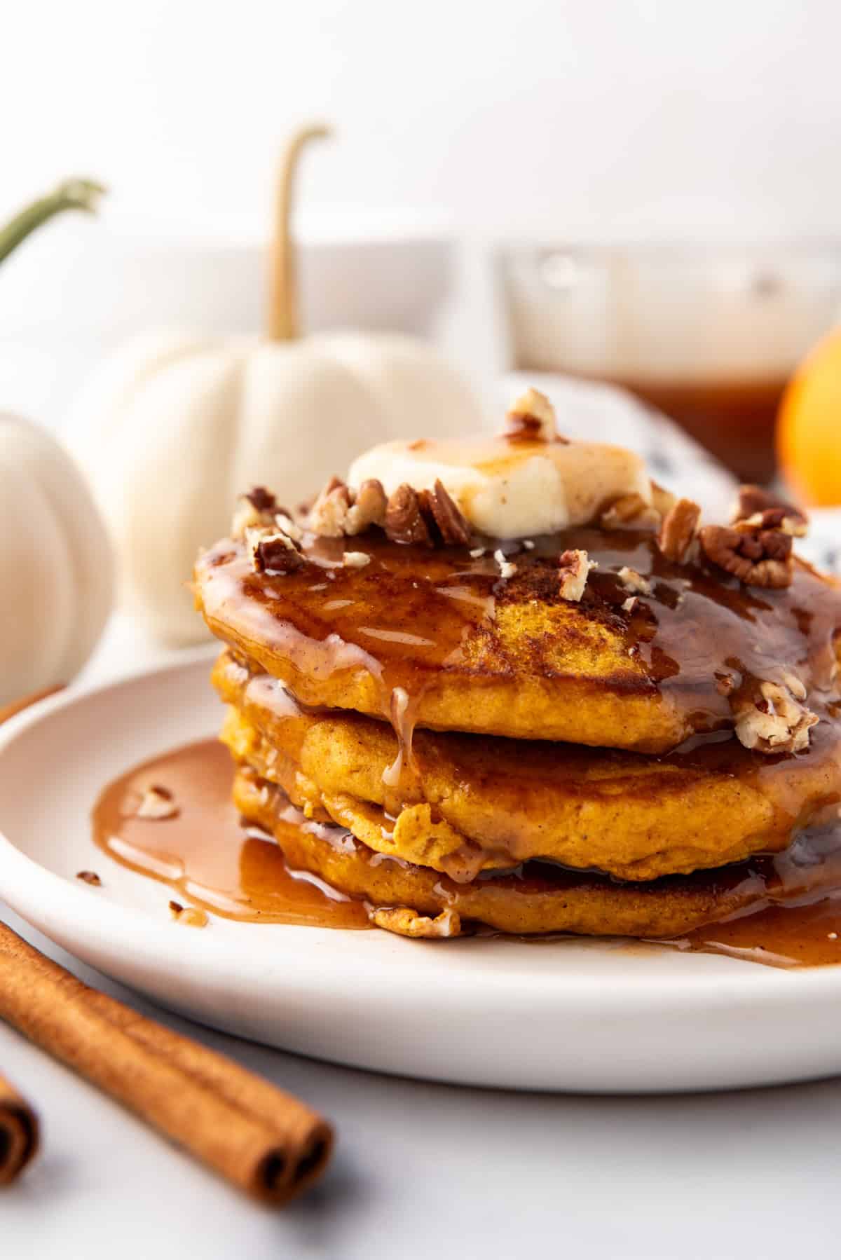 A stack of pumpkin pancakes with cinnamon syrup and chopped pecans on top.