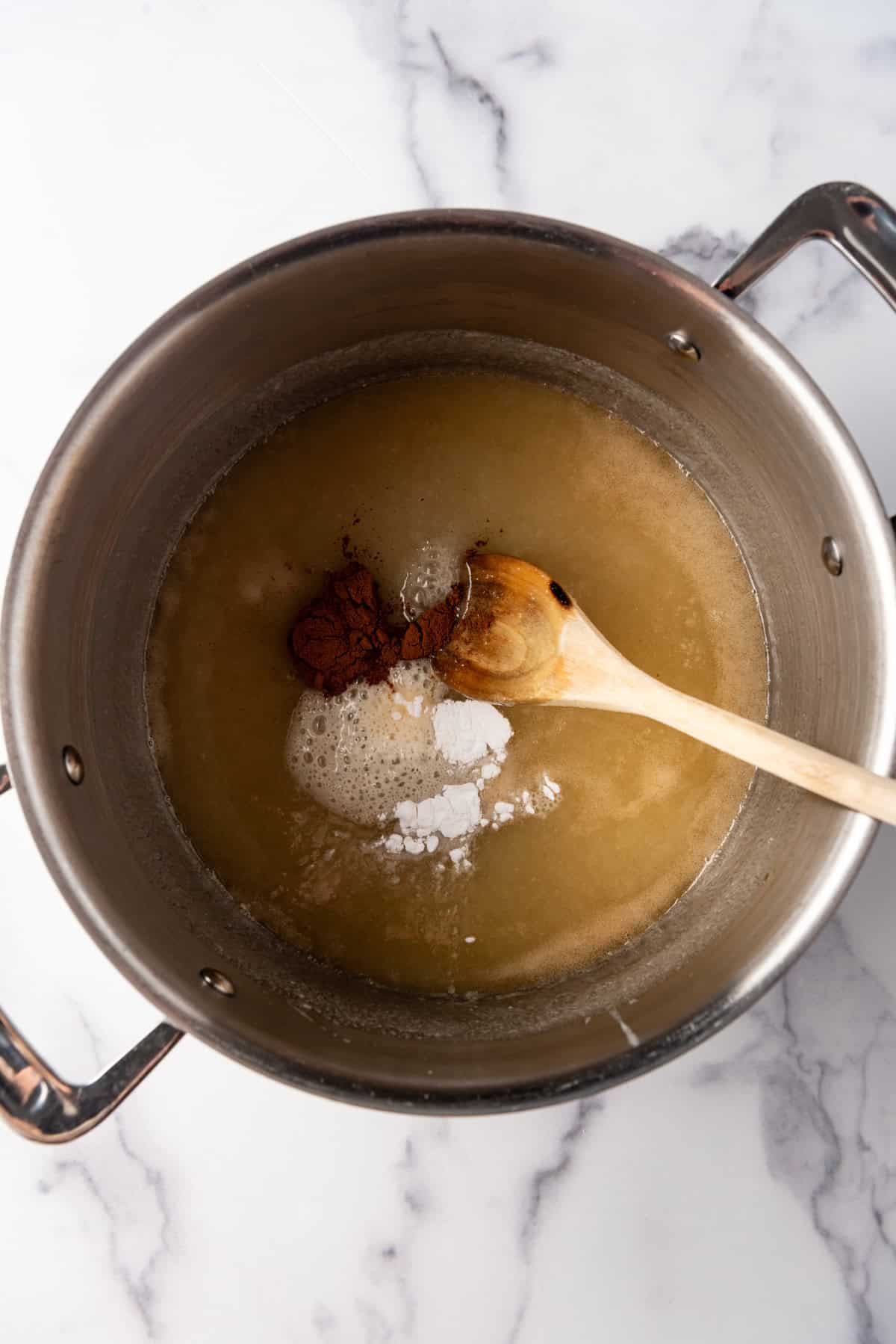 Adding baking soda and cinnamon to creamy buttermilk syrup in a large pot.