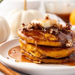 A stack of pumpkin pancakes with cinnamon syrup and chopped pecans on top.