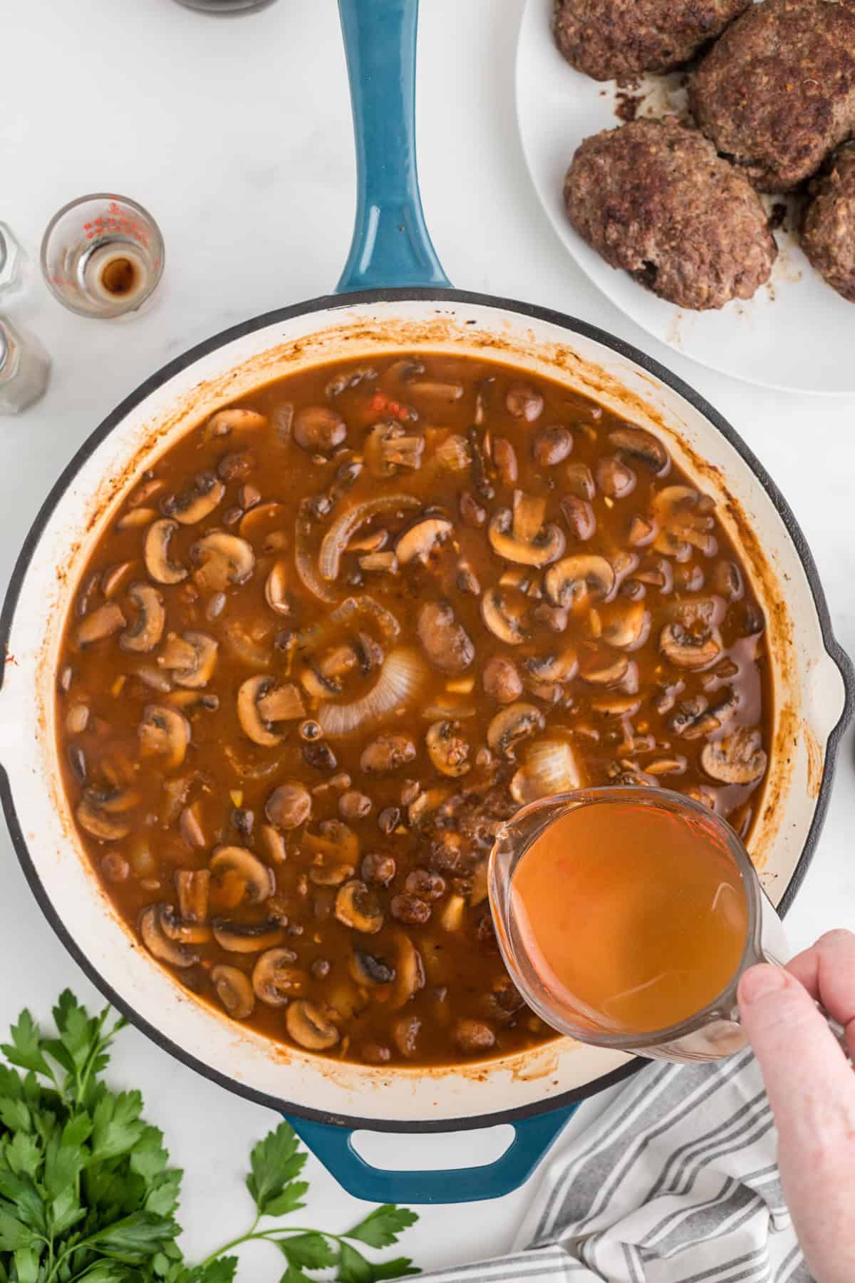 Adding beef broth to a large skillet of sauteed mushrooms and onions.