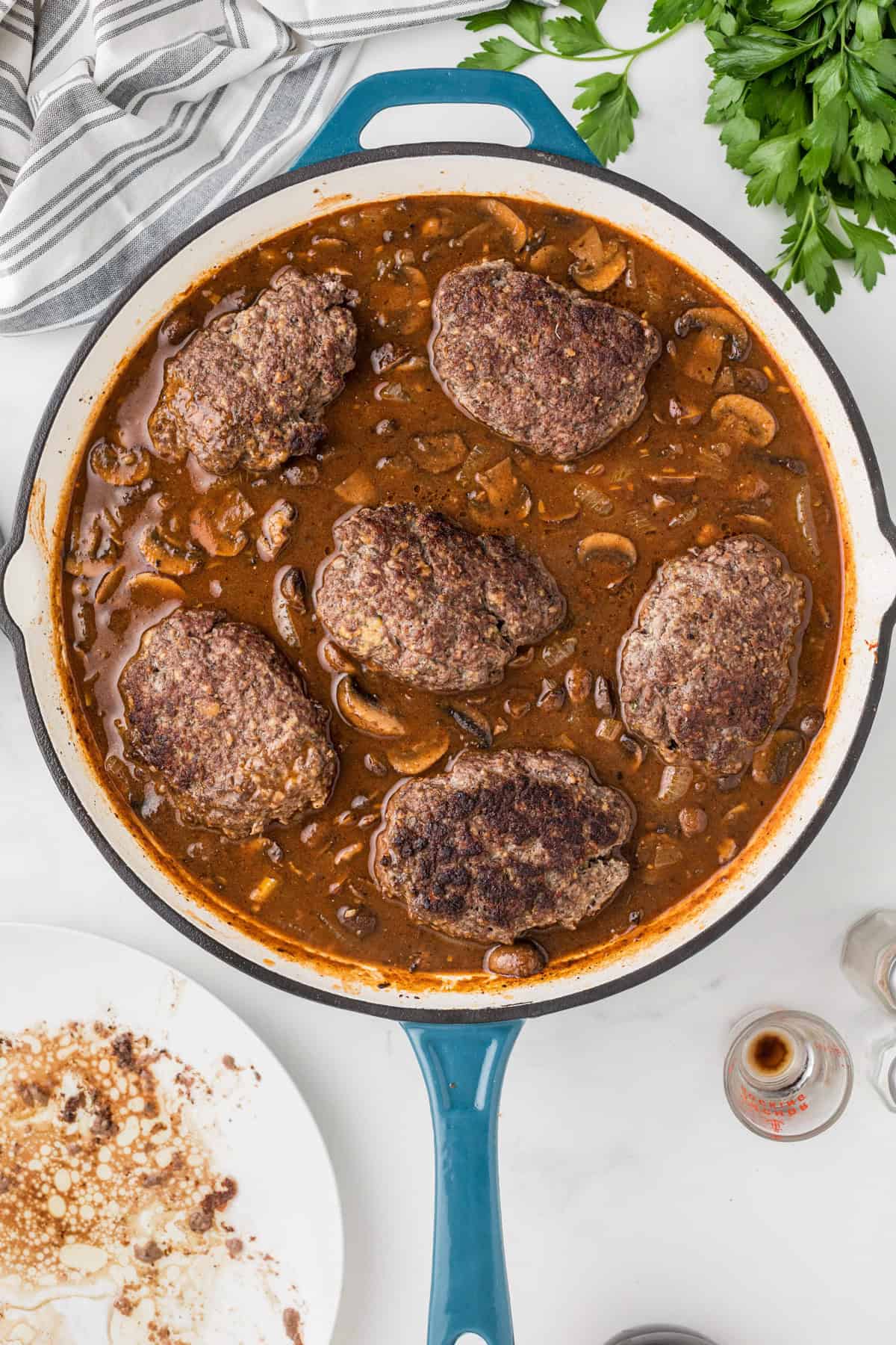 Nestling seared salisbury steaks into a mushroom gravy in a skillet.