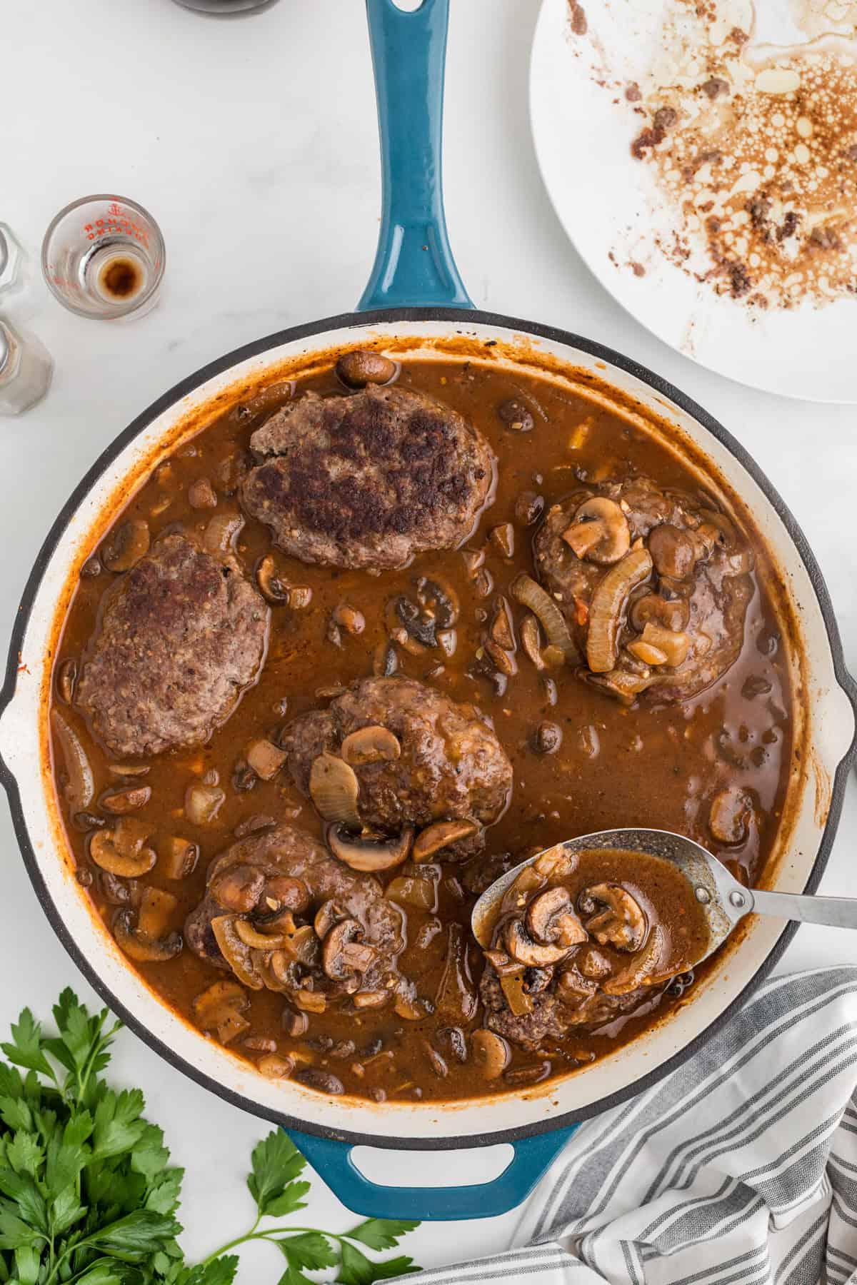 Spooning sauce over salisbury steaks in a pan.