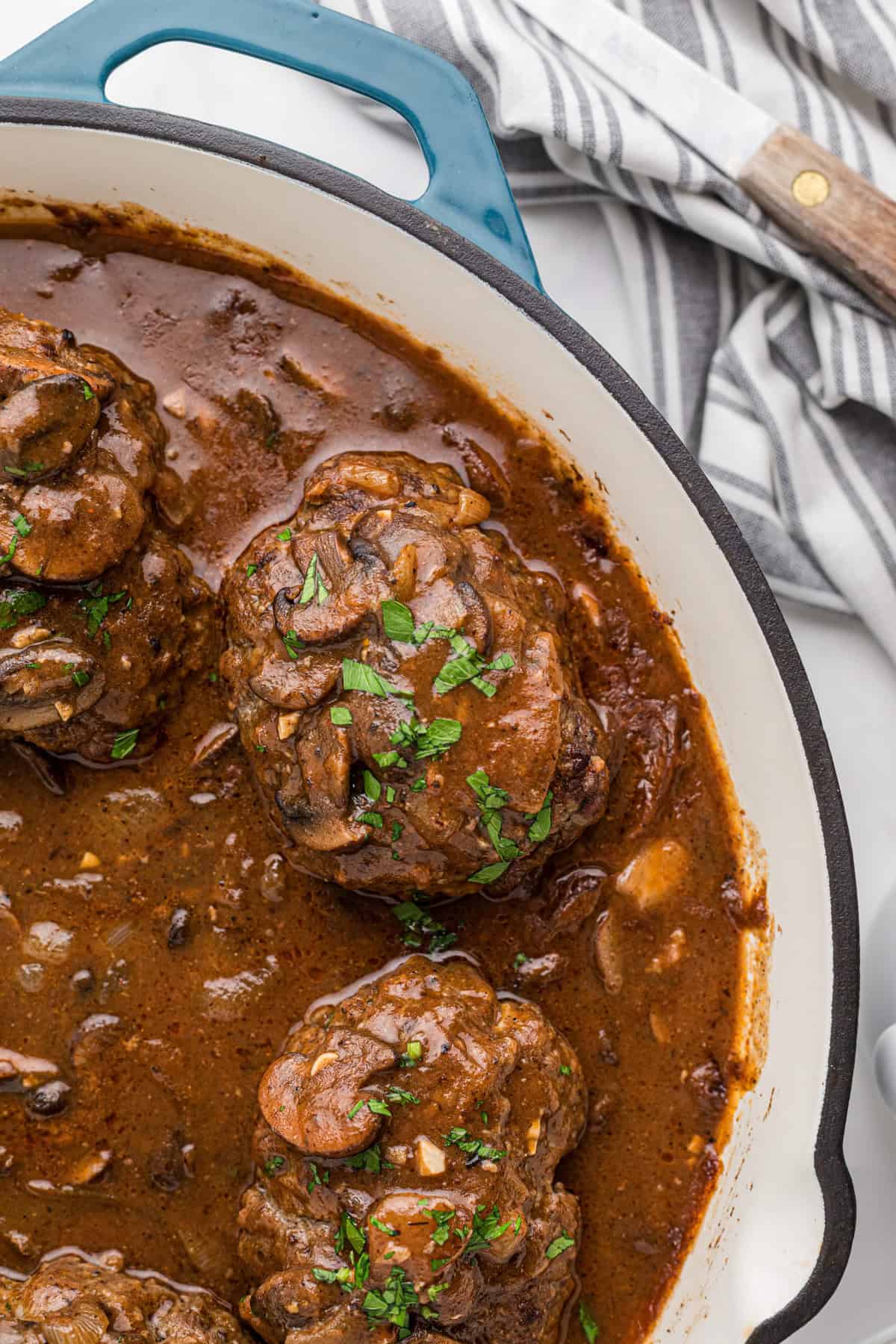 A close up image of finished salisbury steaks garnished with chopped fresh parsley in a pan.