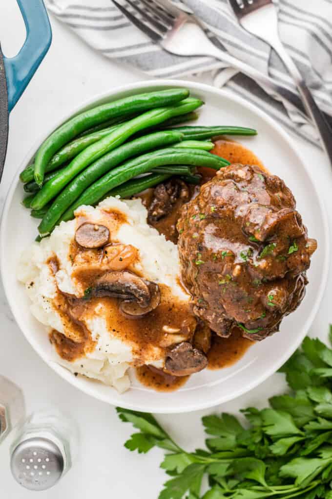 An overhead image of a plate of salisbury steak with mashed potatoes and green beans.