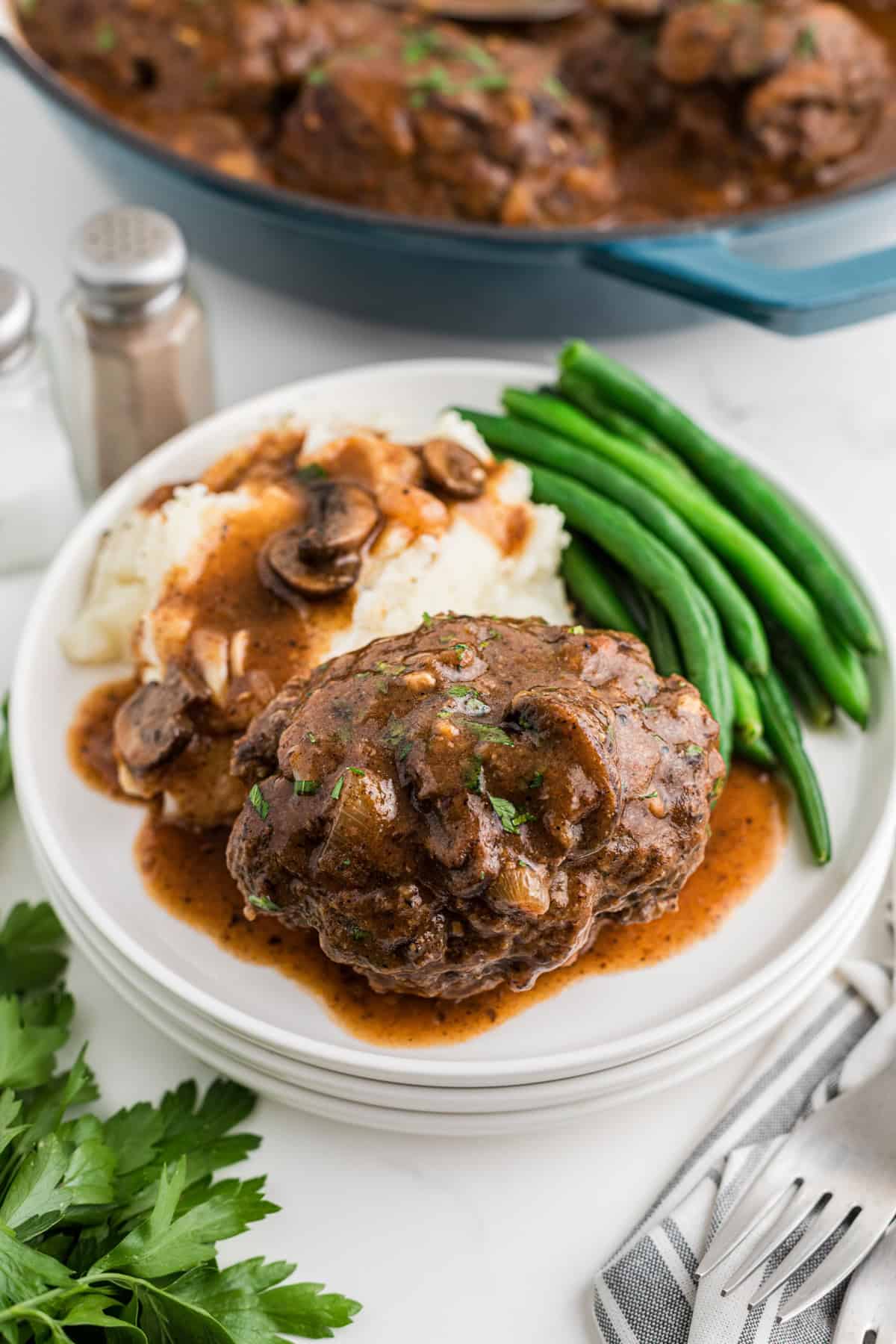 A side view of a white plate with a salisbury steak on it with mashed potatoes and green beans.