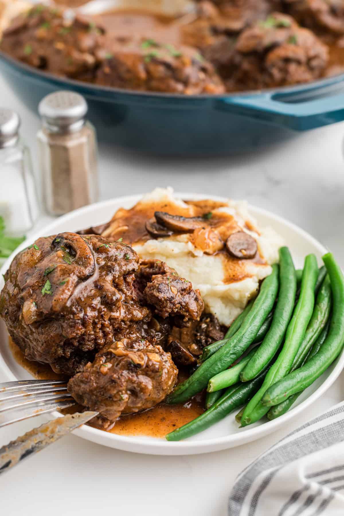 Salisbury steak on a plate with mashed potatoes and green beans.