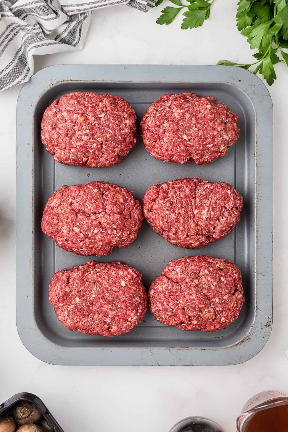 Six shaped salisbury steaks on a pan.