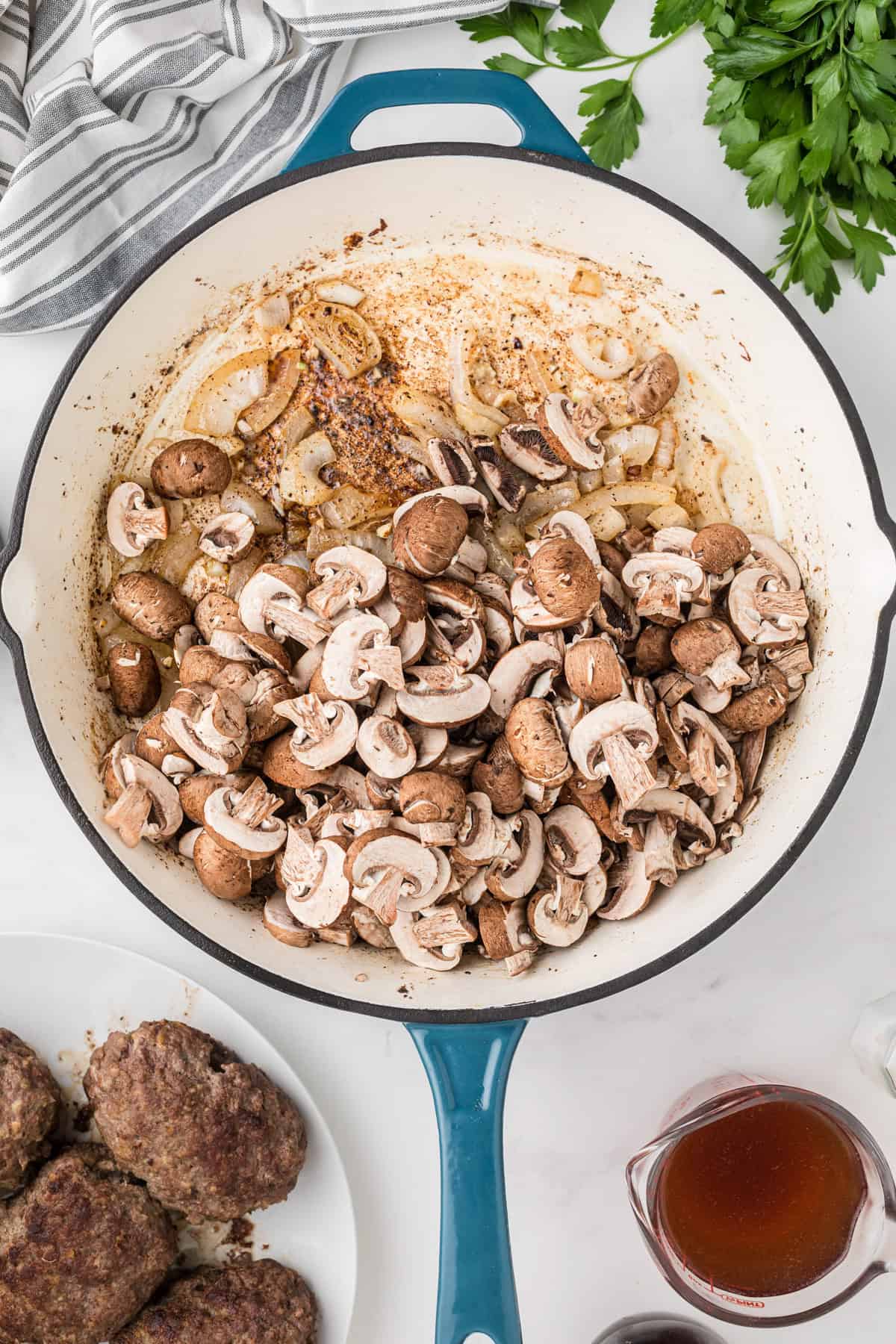 Adding sliced mushrooms to sauteed onions in a large pan.