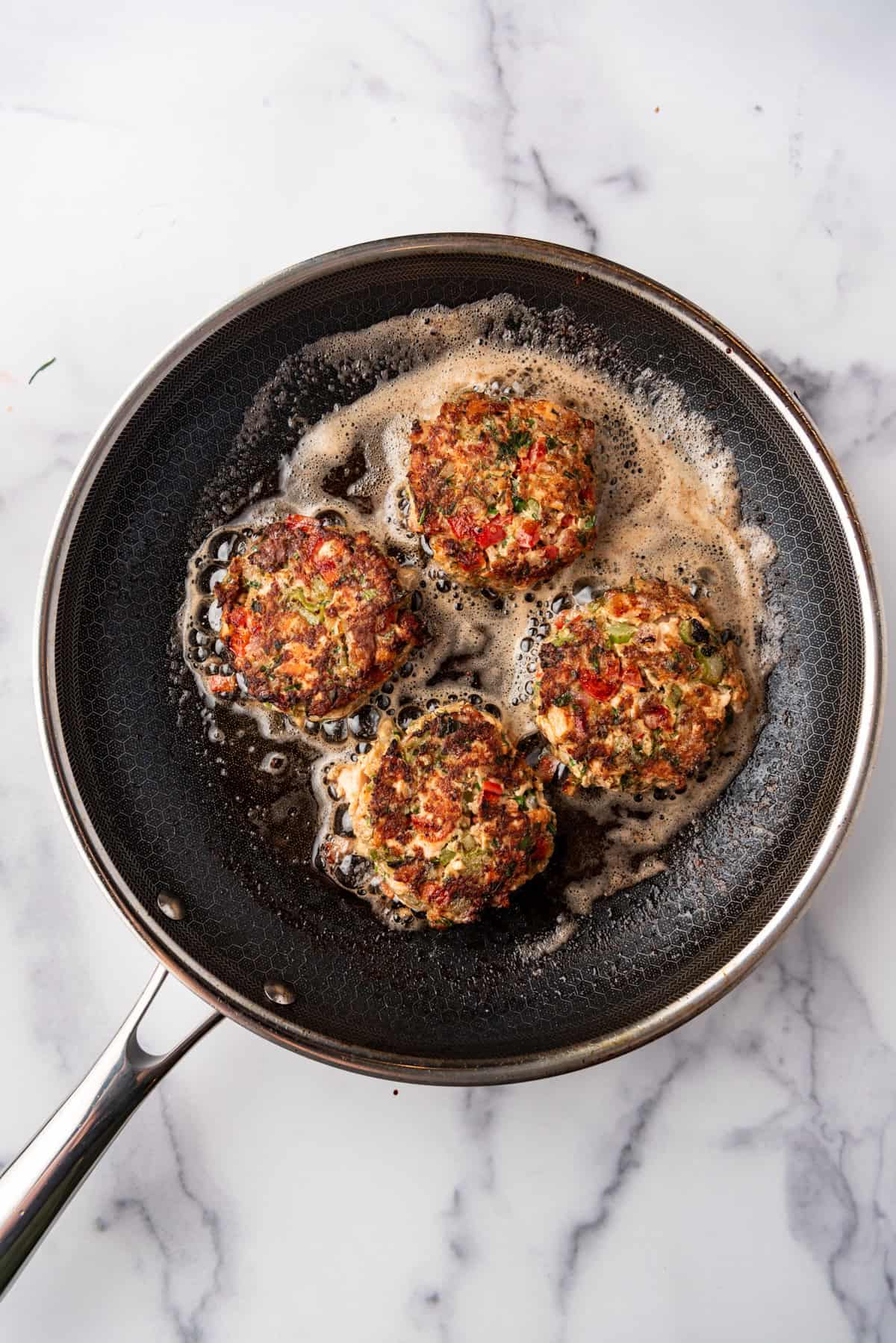 Four Salmon Cakes frying in a skillet.