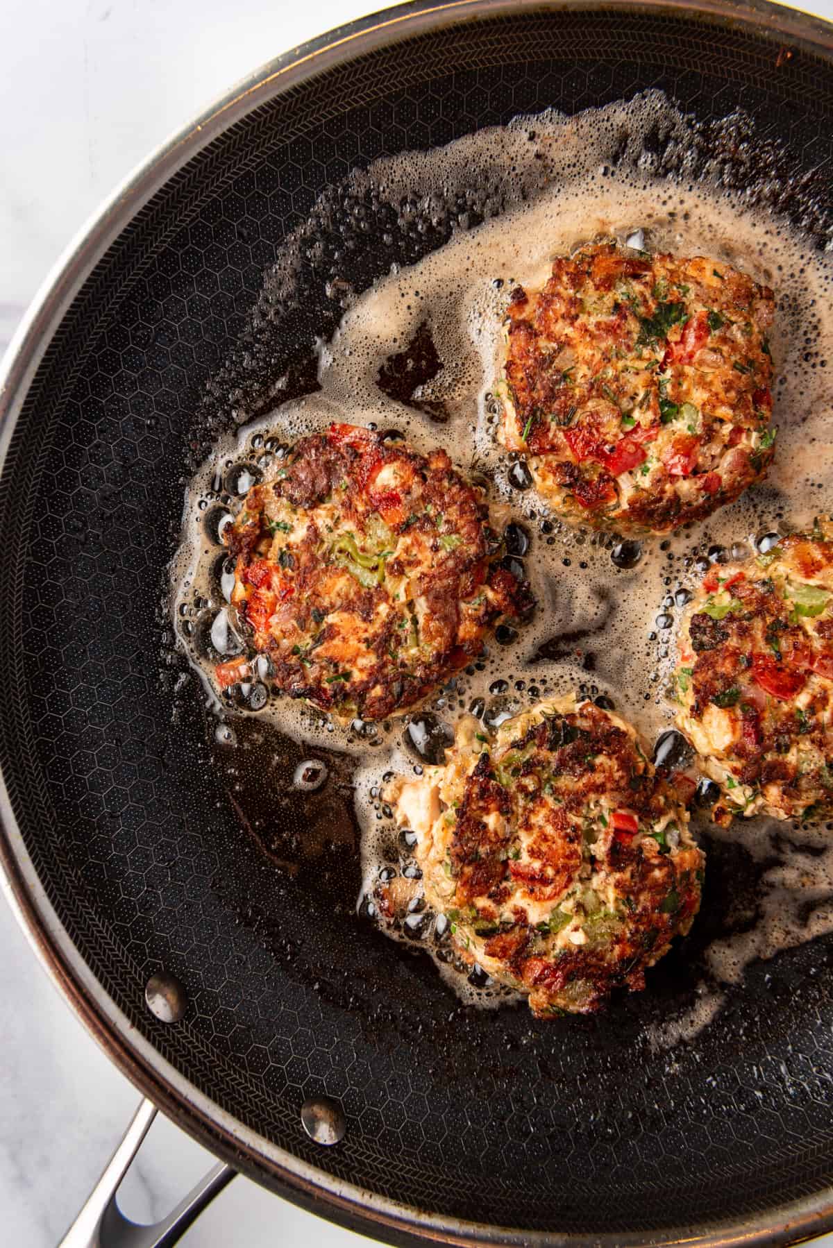 Four Salmon Cakes frying in a skillet.