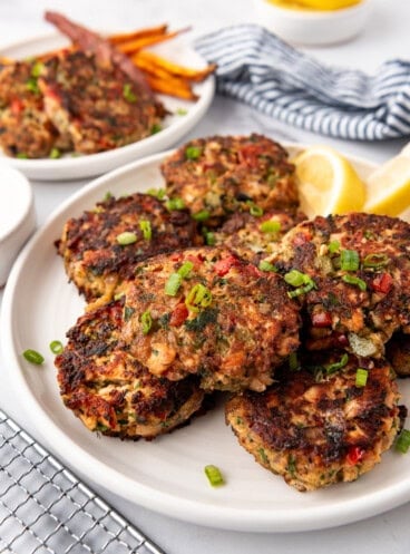 Salmon cakes on a white plate with lemon wedges in the background.