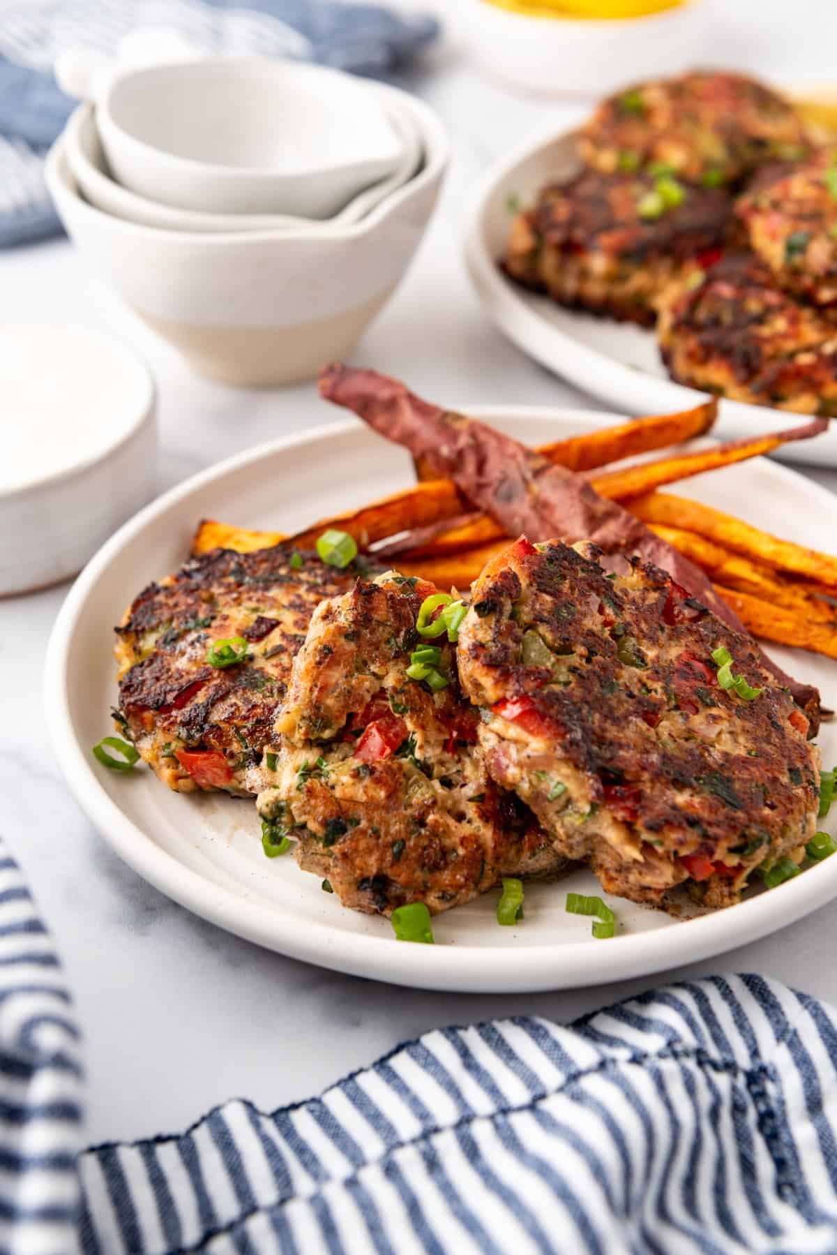 Salmon cakes on a white plate with a side of sweet potato fries.