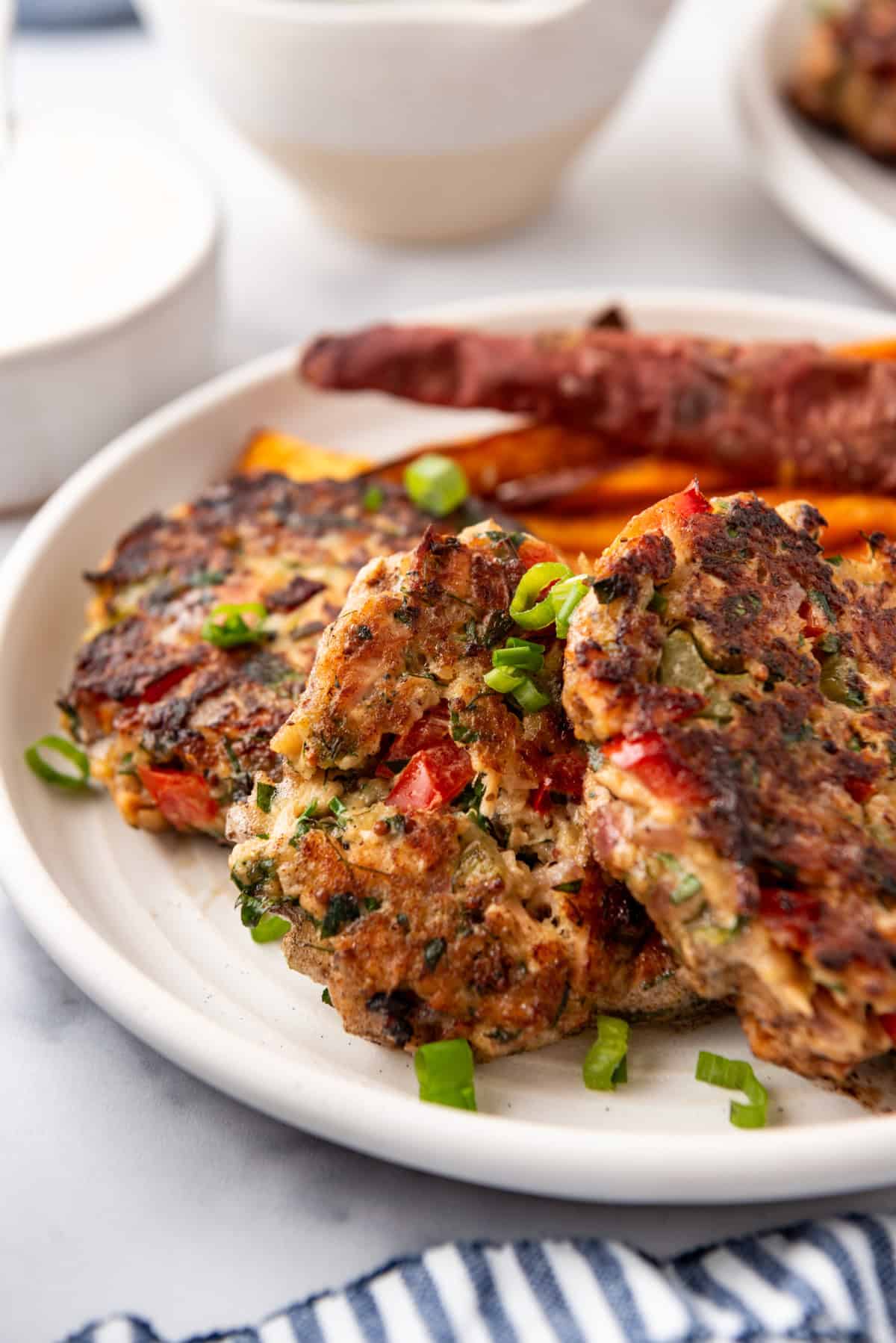 Salmon cakes on a white plate with a side of sweet potato fries.