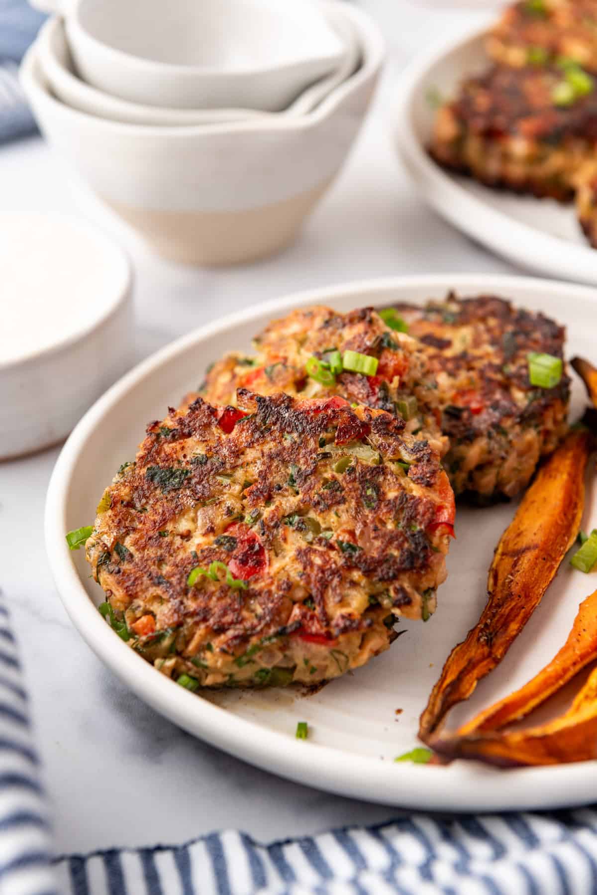 Salmon cakes on a white plate with a side of sweet potato fries.