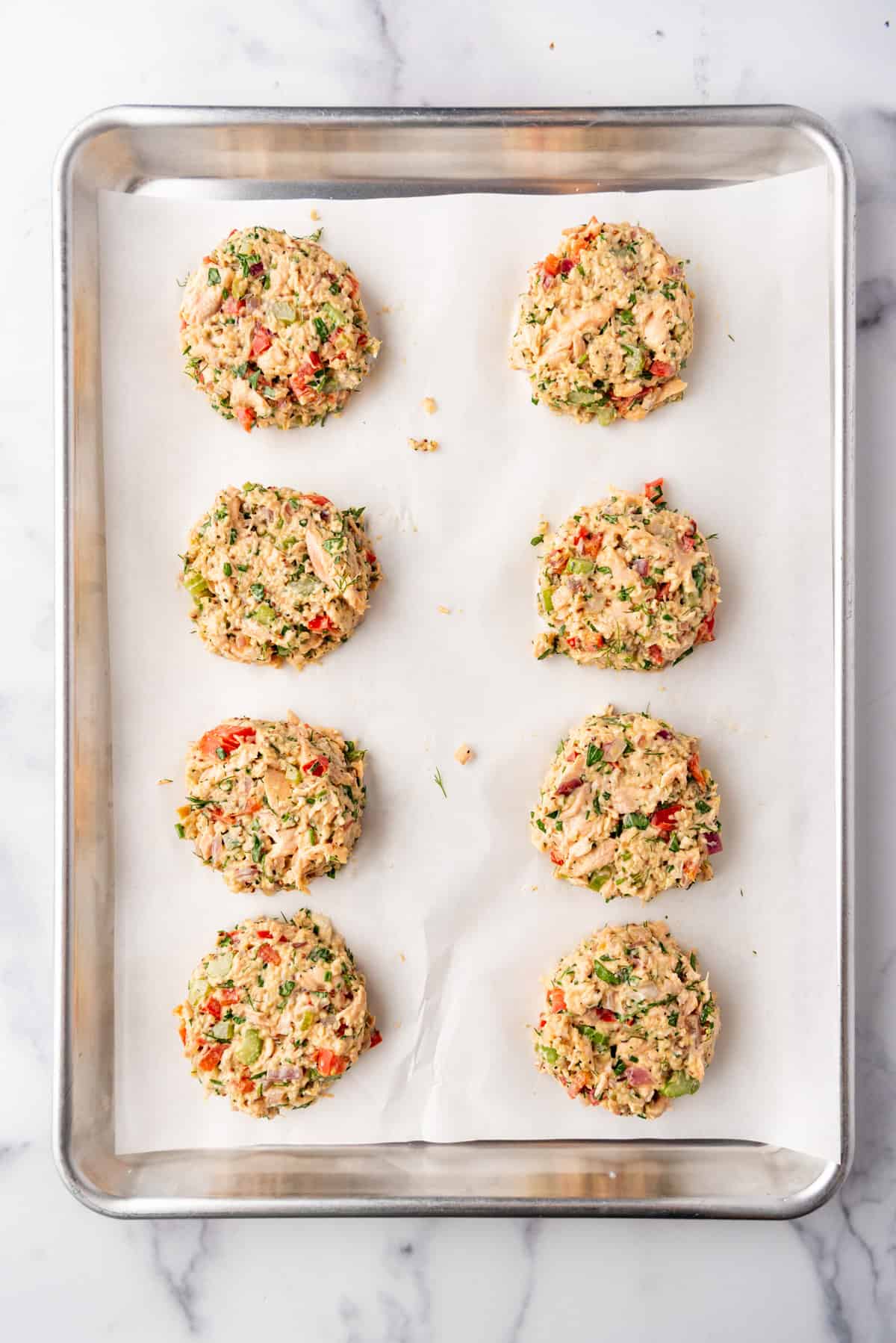 Eight uncooked Salmon Cake patties on a baking sheet lined with parchment paper.