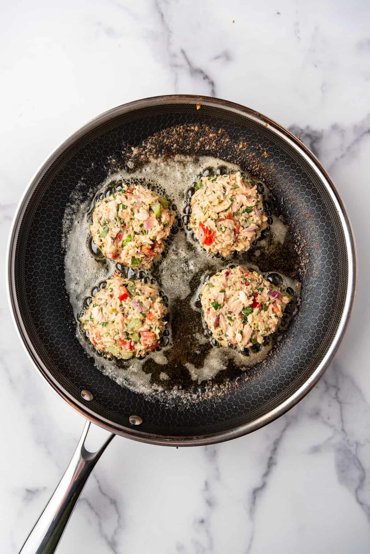 Four uncooked Salmon Cakes frying in a skillet.