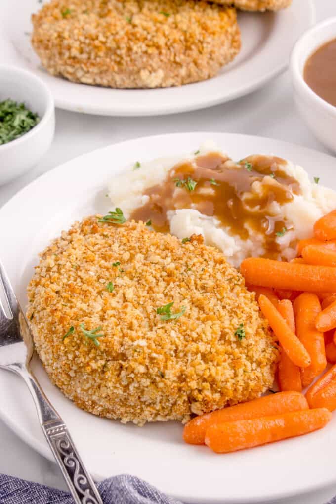 A shake n bake pork chop on a plate with mashed potatoes, gravy, and carrots.