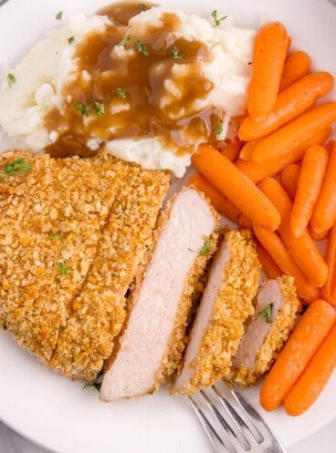 An image of a sliced boneless pork chop on a plate with cooked carrots, mashed potatoes, and gravy.