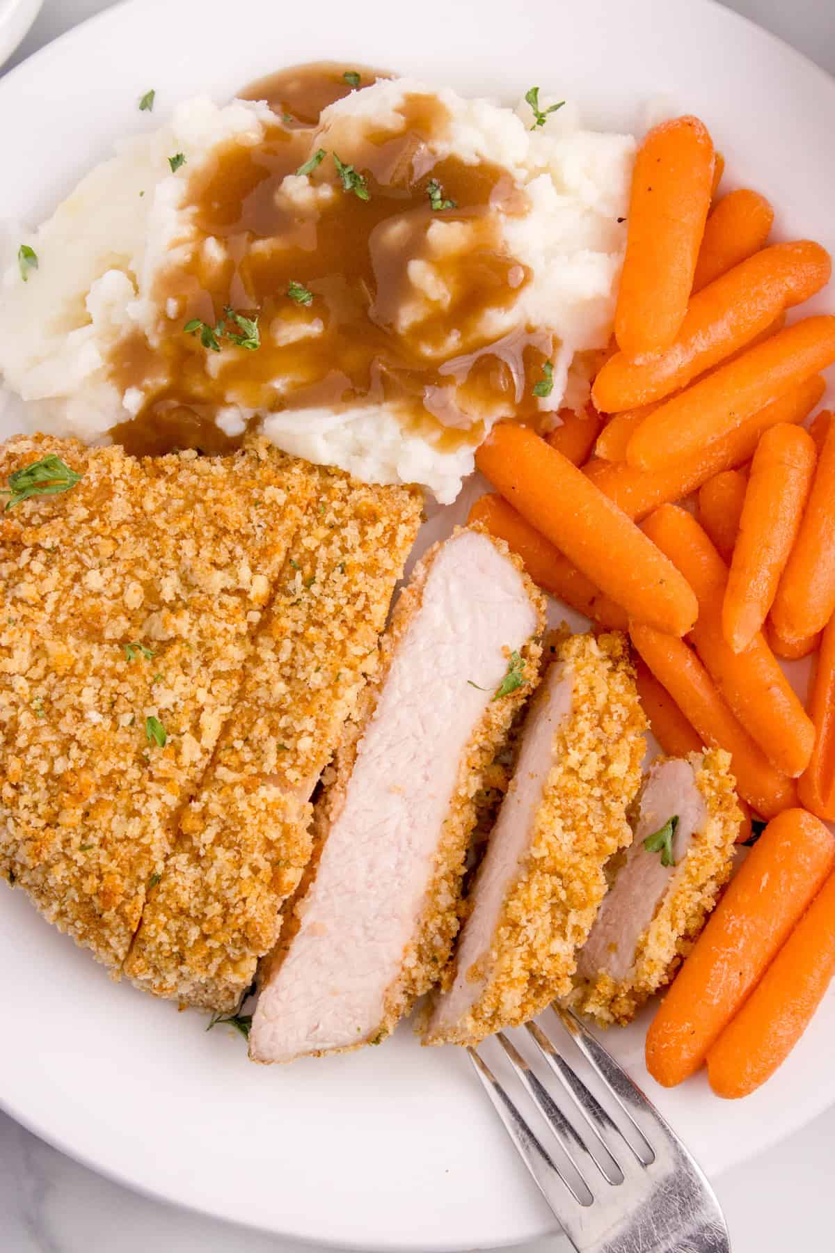 An image of a sliced boneless pork chop on a plate with cooked carrots, mashed potatoes, and gravy.