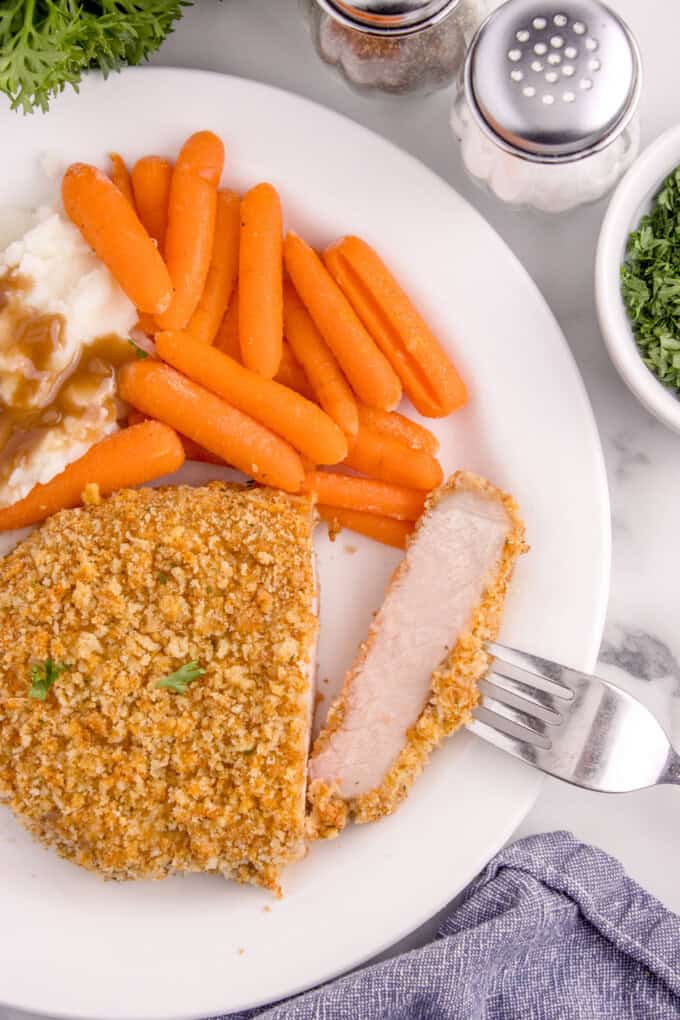 An overhead image of a plate of carrots and breaded pork chop with a fork holding a bite of the pork.