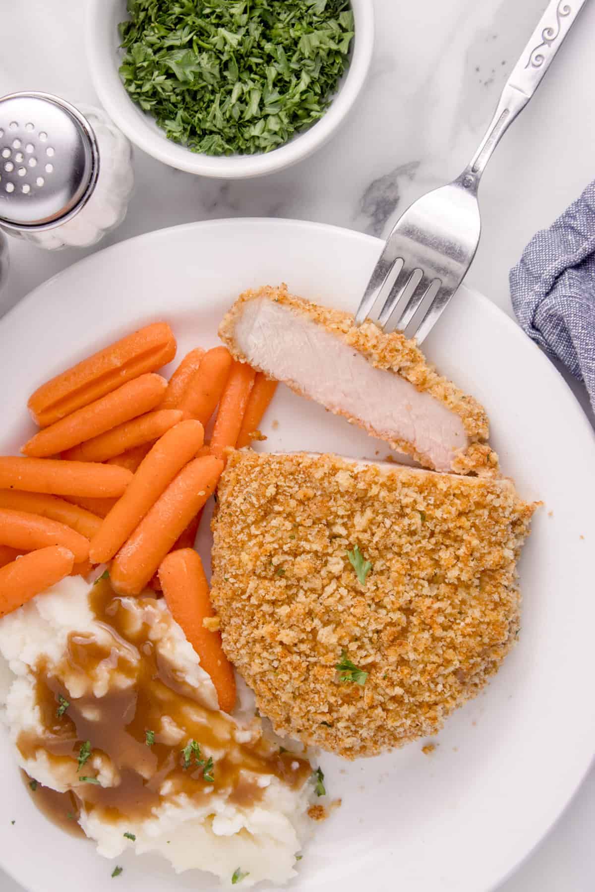 An overhead image of a shake n bake pork chop on a white plate with carrots and mashed potatoes with gravy.