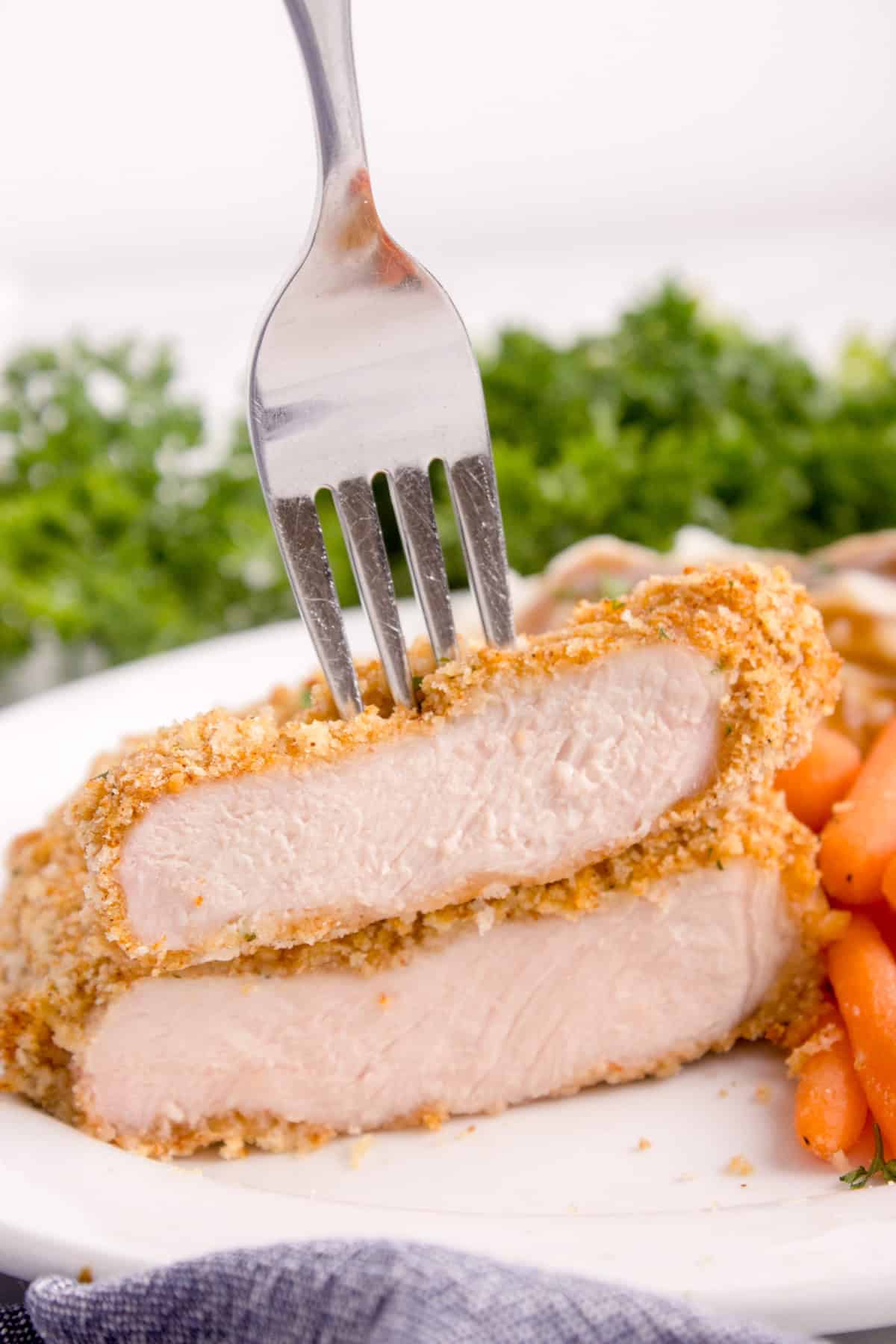 A fork stuck into a piece of tender shake n bake pork chops.