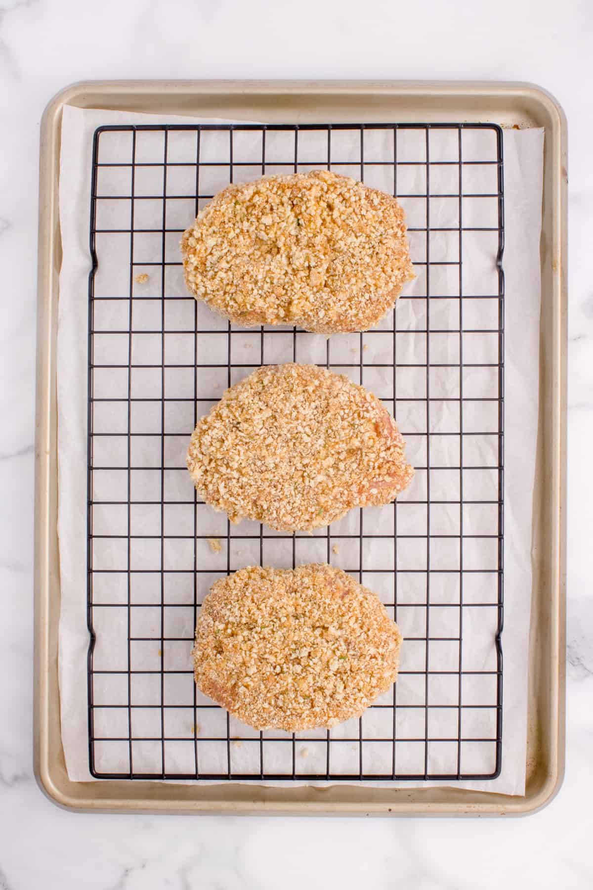 Three breaded pork chops on a wire rack.