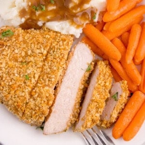 An image of a sliced shake n bake pork chop on a plate with carrots, mashed potatoes, and gravy.