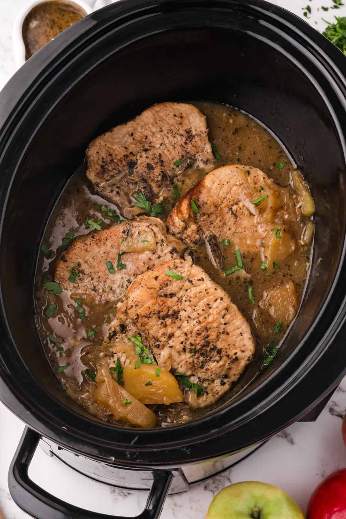 All of the ingredients for making slow cooker apple pork chops combined in a black slow cooker.