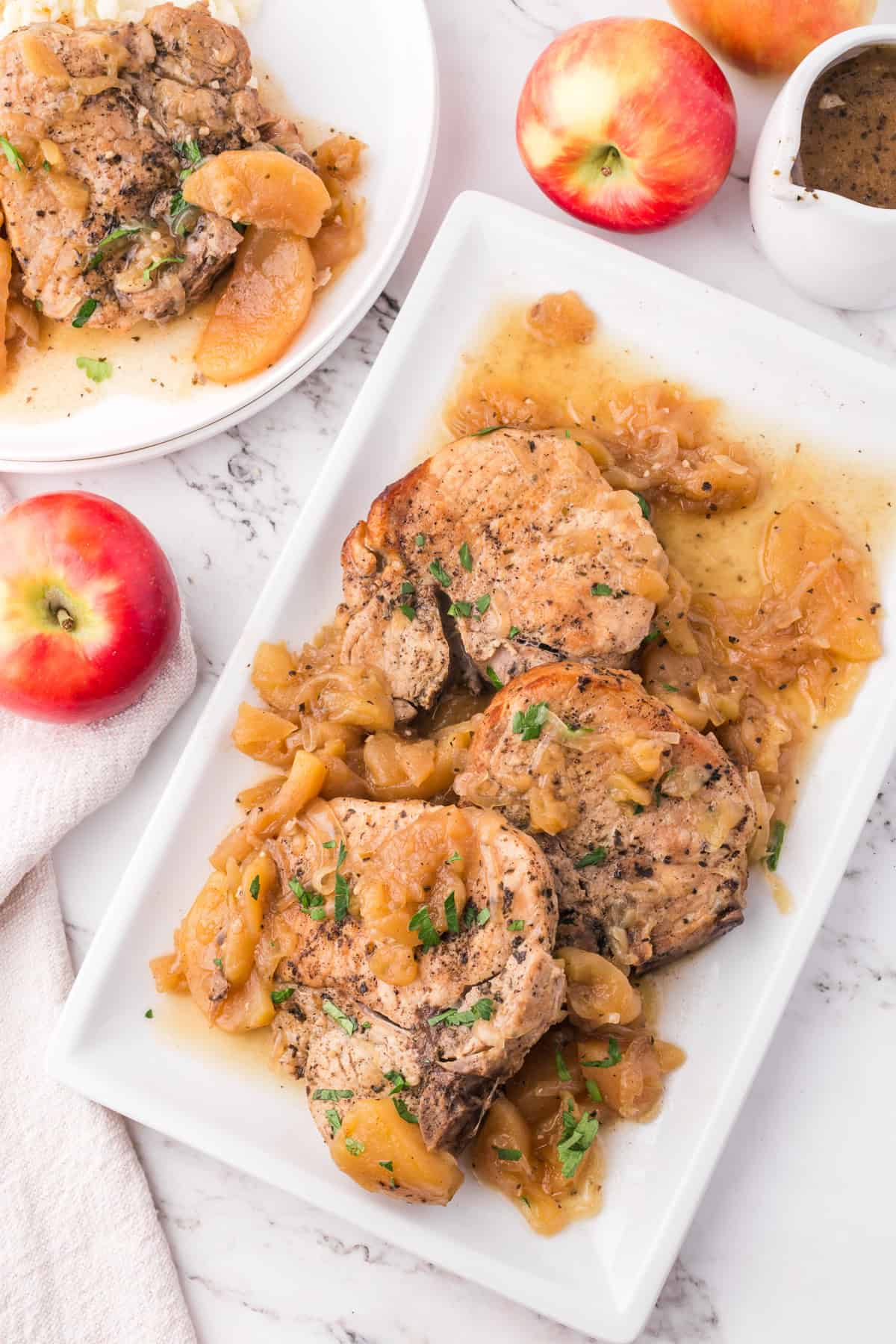 An overhead image of slow cooked pork chops on a plate next to an apple.