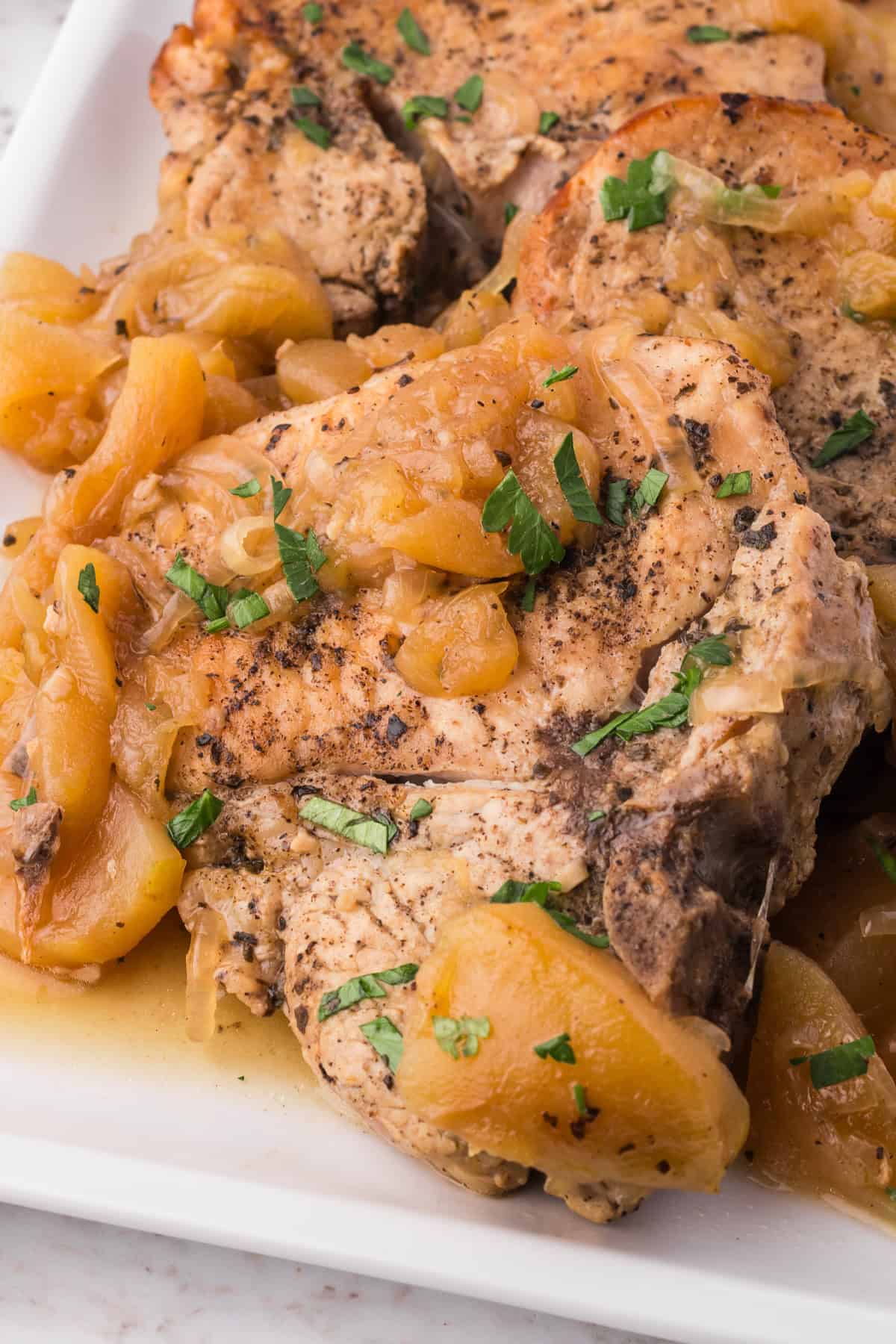 A close up image of a pork chop with apples on a white plate.