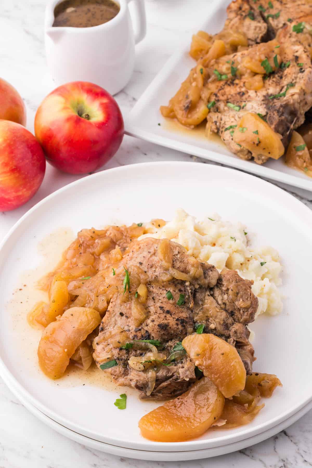 An image of a slow cooker apple pork chop on a plate with mashed potatoes.