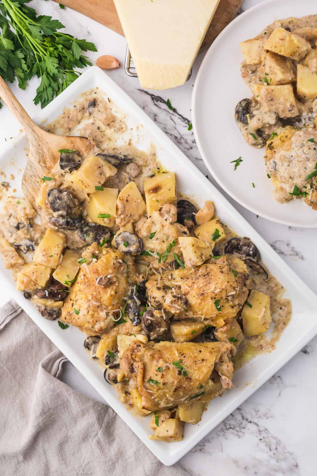 An overhead image of a large rectangular platter of slow cooker chicken thighs with potatoes and  mushrooms.