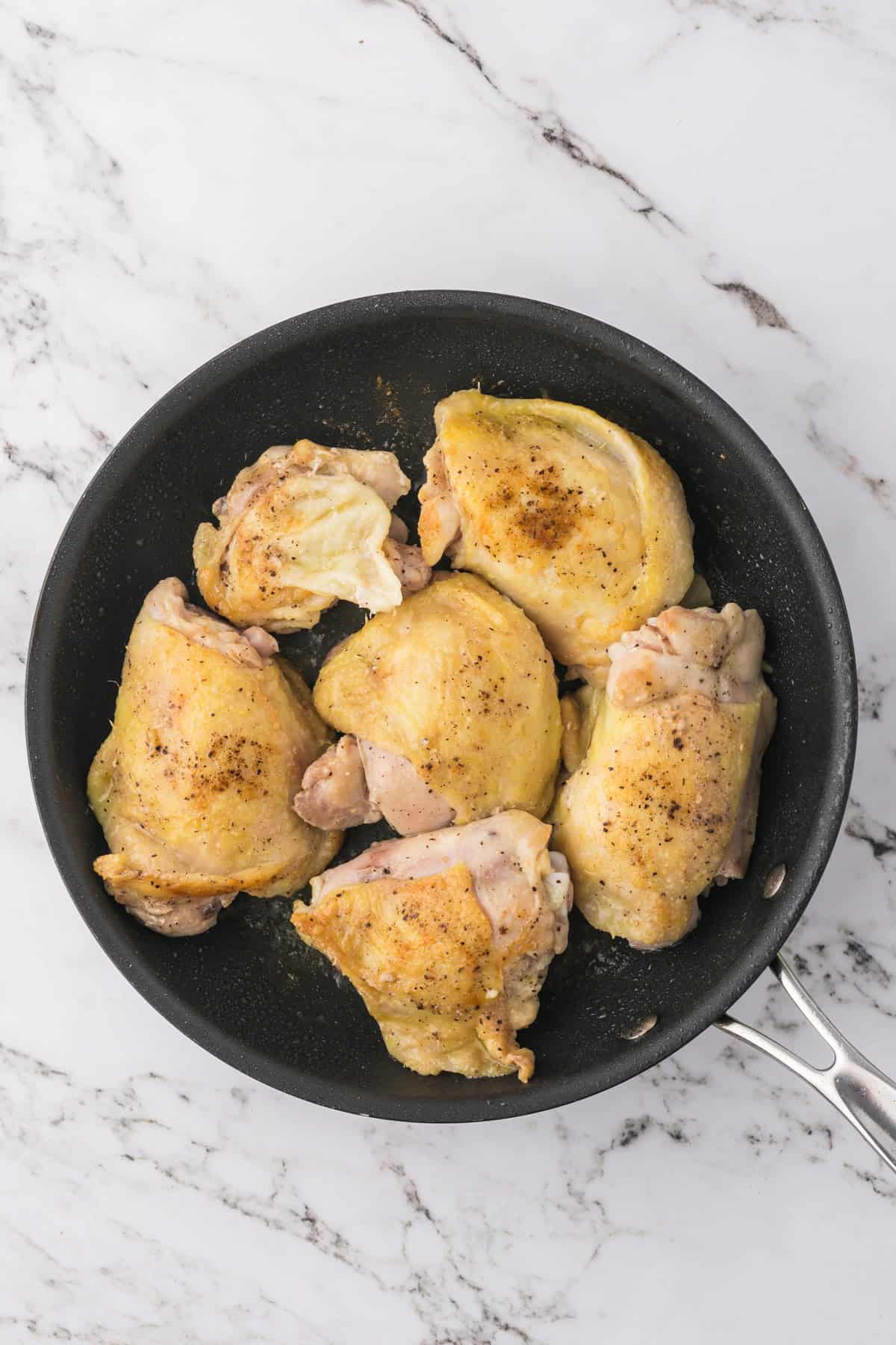 Seared chicken thighs in a pan.