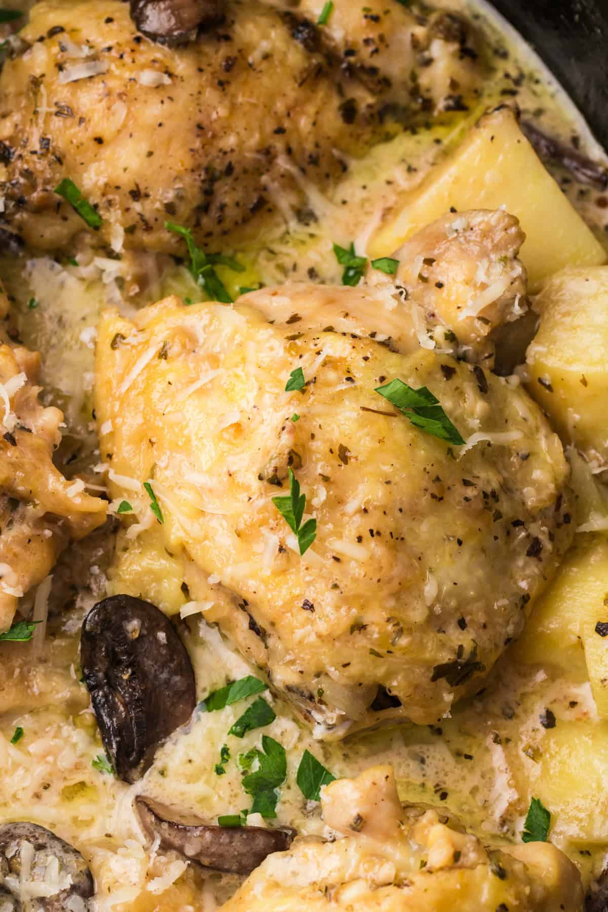 A close up image of a chicken thigh cooked in a slow cooker with  potatoes and mushrooms.