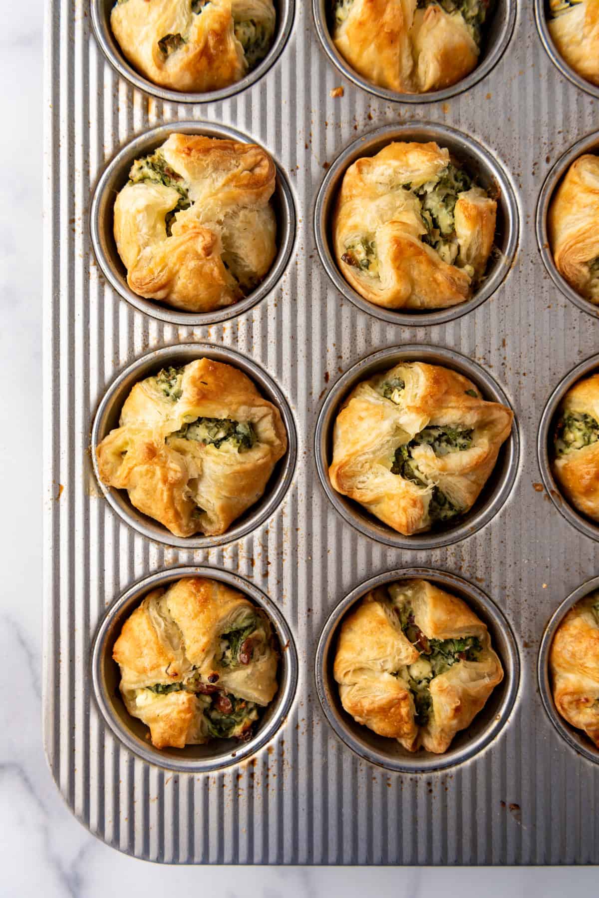 An overhead image of baked spinach puffs in a muffin pan.