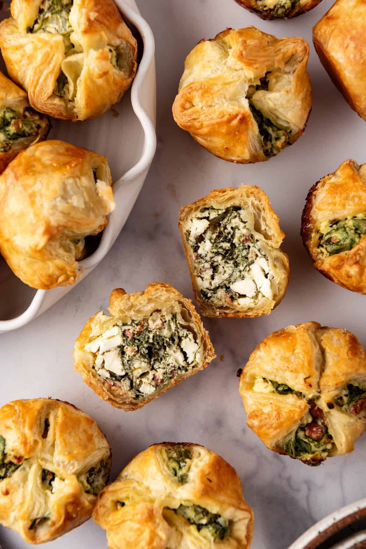 A spinach puff that has been sliced in half surrounded by more whole spinach puffs.